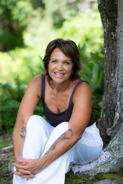 Cindy Capwell, the yoga and meditation teacher behind Missing Peace Yoga, smiling outdoors by a tree.