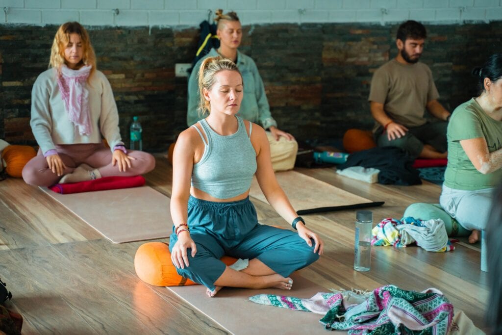 Group seated in meditation on mats in a softly lit studio during a yoga and breathwork class in Palm City Florida