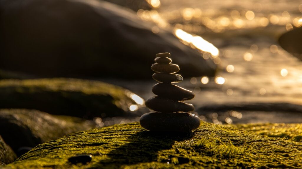 Balanced stones beside a stream at sunset, evoking private yoga, meditation and breathwork sessions.